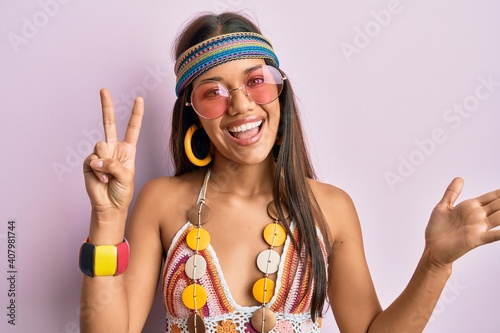 Beautiful hispanic woman wearing bohemian and hippie style doing peace symbol celebrating achievement with happy smile and winner expression with raised hand