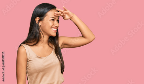 Beautiful hispanic woman wearing casual clothes very happy and smiling looking far away with hand over head. searching concept.