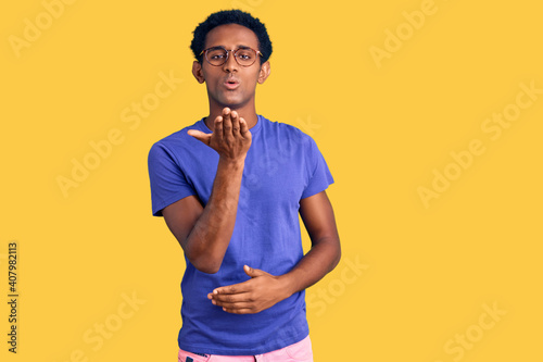 African handsome man wearing casual clothes and glasses looking at the camera blowing a kiss with hand on air being lovely and sexy. love expression.
