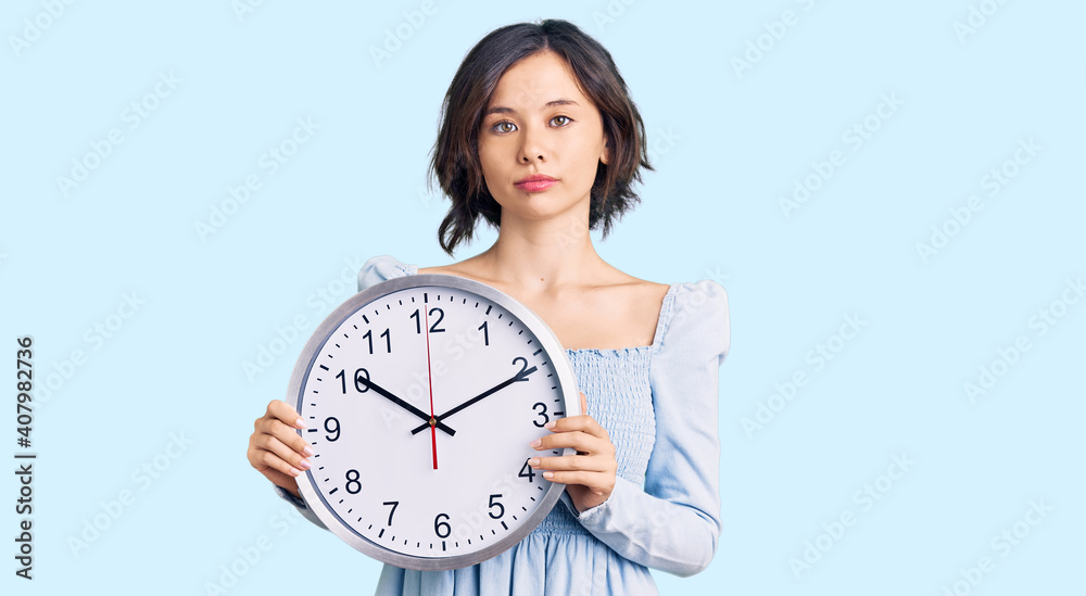 Young beautiful girl holding big clock thinking attitude and sober expression looking self confident Young beautiful girl holding big clock thinking attitude and sober expression looking self confident