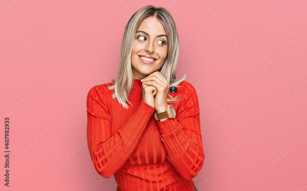 Beautiful blonde woman wearing casual clothes laughing nervous and excited with hands on chin looking to the side Beautiful blonde woman wearing casual clothes laughing nervous and excited with hands on chin looking to the side