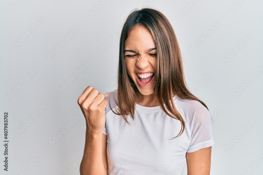Young brunette woman wearing casual white t shirt celebrating surprised and amazed for success with arms raised and eyes closed Young brunette woman wearing casual white t shirt celebrating surprised and amazed for success with arms raised and eyes closed