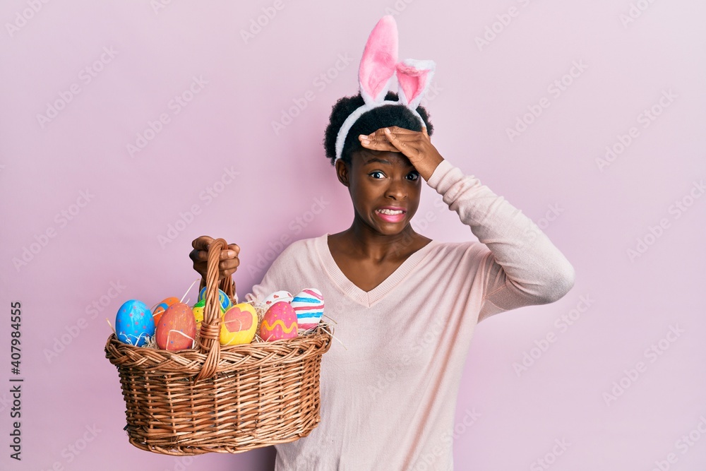 Young african american girl wearing cute easter bunny ears holding basket with painted eggs stressed and frustrated with hand on head, surprised and angry face Young african american girl wearing cute easter bunny ears holding basket with painted eggs stressed and frustrated with hand on head, surprised and angry face