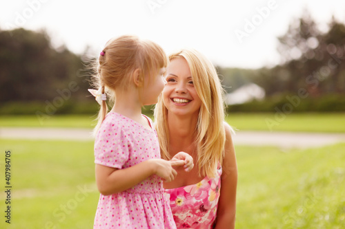 Young blonde mother in dress playing with little kid blonde daughter in the park.