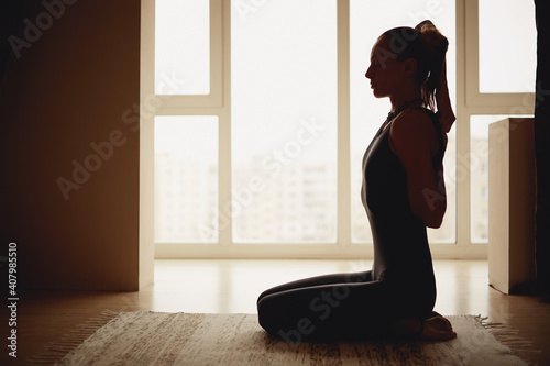 Middle age blond woman doing yoga at home near the window.