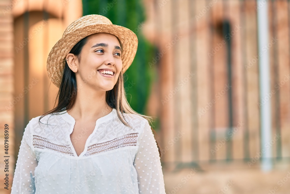 Young hispanic tourist woman wearing summer hat standing at the city.