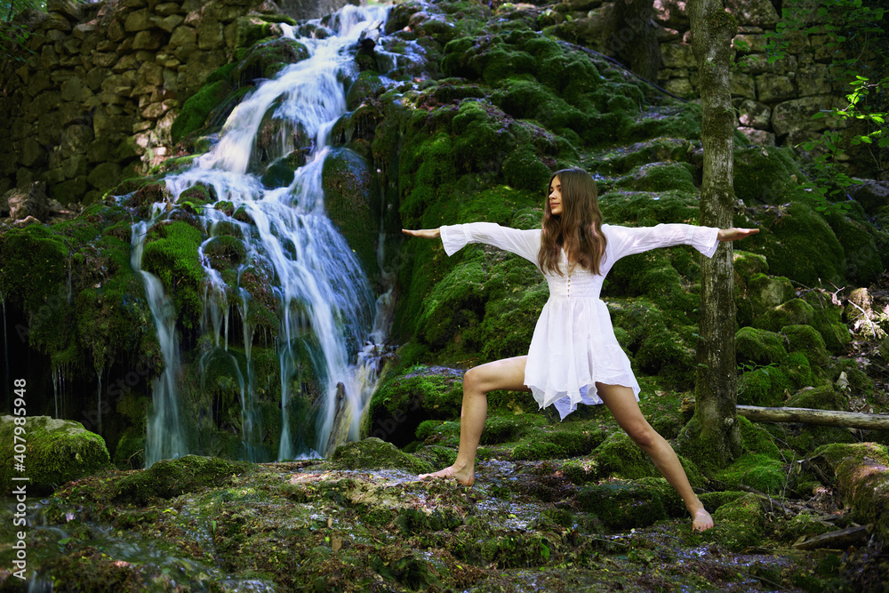 Young caucasian woman in white dress doing yoga near a waterfall in the mountains. Young caucasian woman in white dress doing yoga near a waterfall in the mountains.