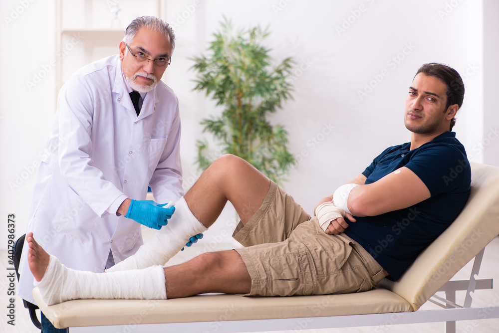 Obraz premium Young injured man visiting old doctor traumatologist