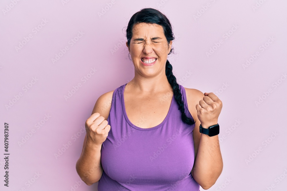Plus size brunette woman wearing sportswear celebrating surprised and amazed for success with arms raised and eyes closed Plus size brunette woman wearing sportswear celebrating surprised and amazed for success with arms raised and eyes closed