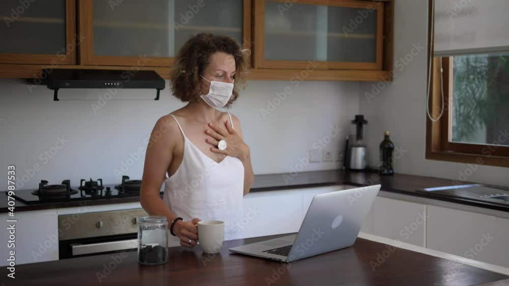 Caucasian girl in face mask video chatting and drinking tea at the kitchen. Staying connected during quarantine Caucasian girl in face mask video chatting and drinking tea at the kitchen. Staying connected during quarantine
