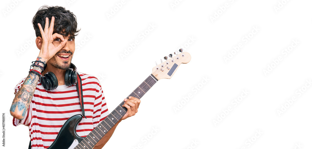 Young hispanic man playing electric guitar smiling happy doing ok sign with hand on eye looking through fingers Young hispanic man playing electric guitar smiling happy doing ok sign with hand on eye looking through fingers