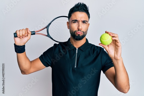 Young man with beard playing tennis holding racket and ball looking at the camera blowing a kiss being lovely and sexy. love expression. © Krakenimages.com