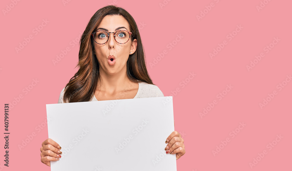 Young brunette woman holding blank empty banner scared and amazed with open mouth for surprise, disbelief face Young brunette woman holding blank empty banner scared and amazed with open mouth for surprise, disbelief face