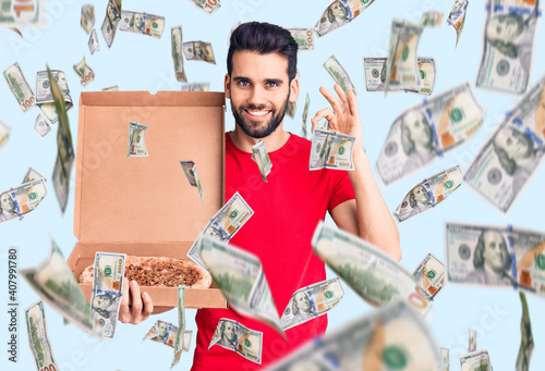 Young handsome man with beard holding delivery cardoboard with italian pizza doing ok sign with fingers, smiling friendly gesturing excellent symbol photo