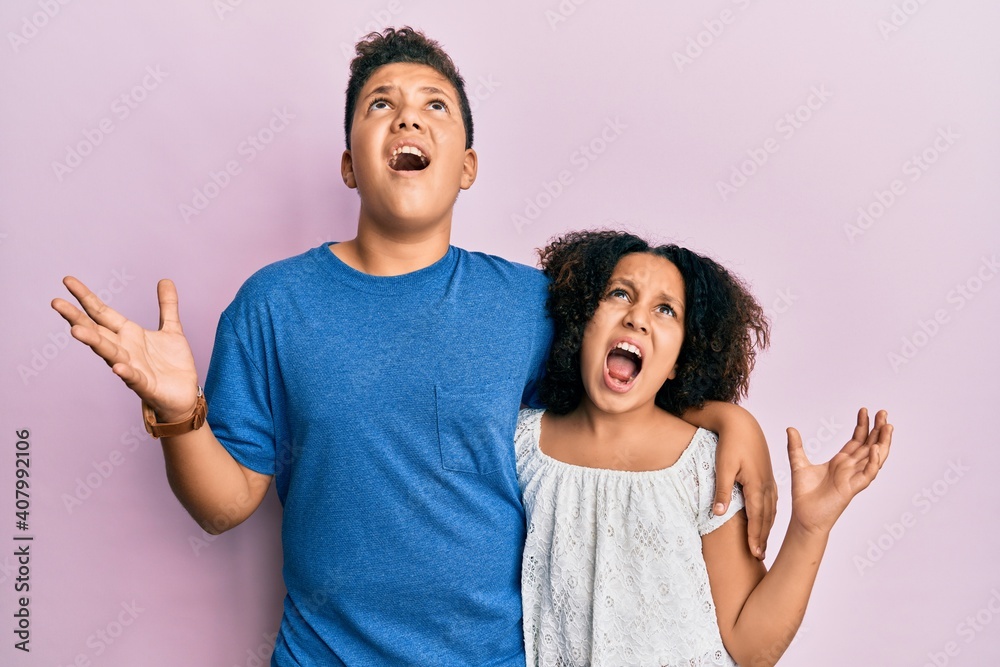 Obraz premium Young hispanic family of brother and sister wearing casual clothes together crazy and mad shouting and yelling with aggressive expression and arms raised. frustration concept.
