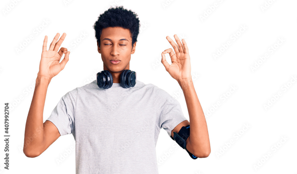Young african american man wearing gym clothes and using headphones relax and smiling with eyes closed doing meditation gesture with fingers. yoga concept. Young african american man wearing gym clothes and using headphones relax and smiling with eyes closed doing meditation gesture with fingers. yoga concept.