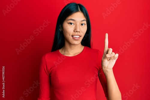 Young chinese woman wearing casual clothes smiling with an idea or question pointing finger up with happy face  number one