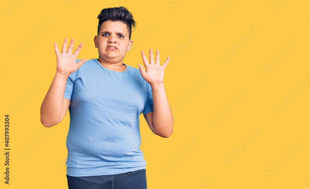 Little boy kid wearing sports workout clothes afraid and terrified with fear expression stop gesture with hands, shouting in shock. panic concept. Little boy kid wearing sports workout clothes afraid and terrified with fear expression stop gesture with hands, shouting in shock. panic concept.
