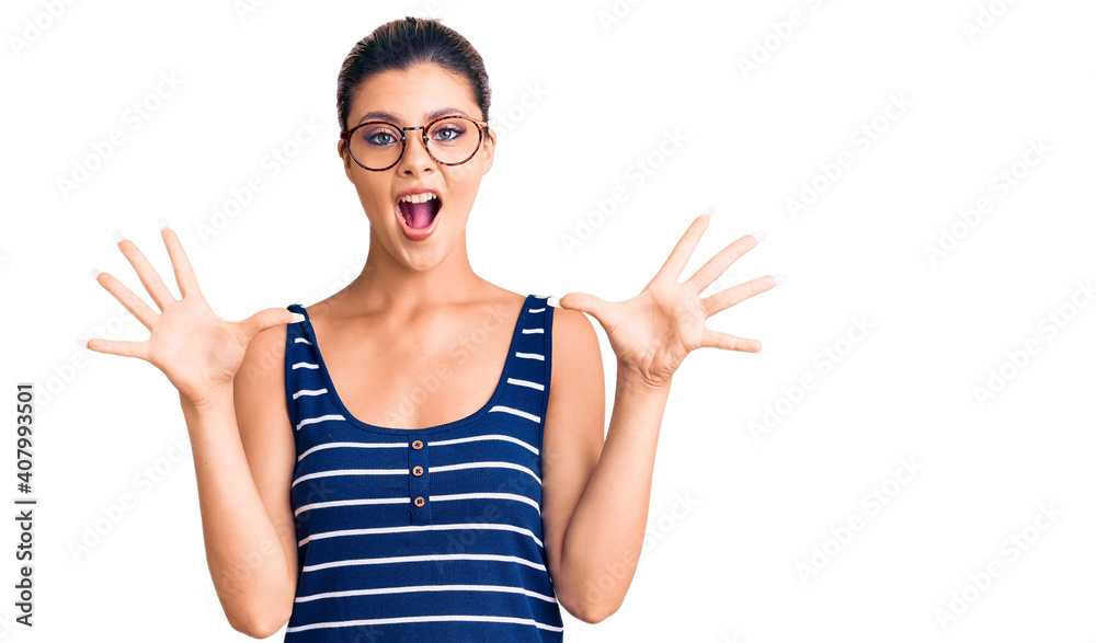 Young beautiful woman wearing casual clothes and glasses celebrating crazy and amazed for success with arms raised and open eyes screaming excited. winner concept Young beautiful woman wearing casual clothes and glasses celebrating crazy and amazed for success with arms raised and open eyes screaming excited. winner concept