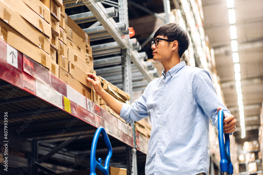 Portrait of smiling asian manager worker man standing and order details checking goods and supplies on shelves with cardboard box goods background in warehouse.logistic and business export Portrait of smiling asian manager worker man standing and order details checking goods and supplies on shelves with cardboard box goods background in warehouse.logistic and business export