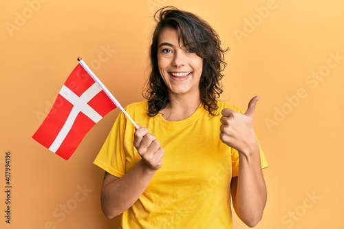 Canvas Print Young hispanic woman holding denmark flag smiling happy and positive, thumb up d