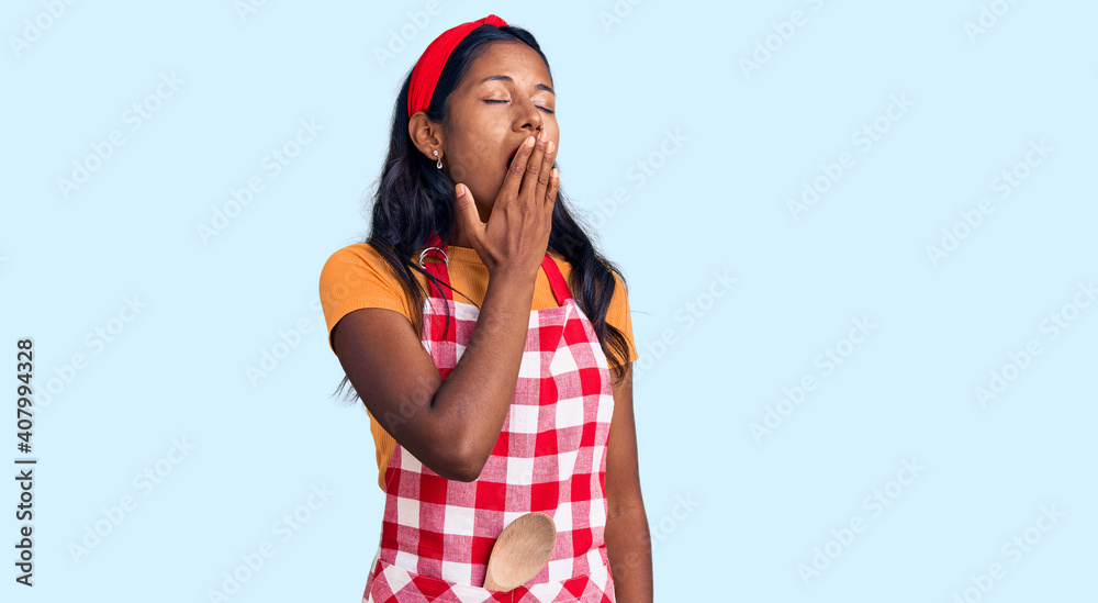 Young indian girl wearing professional baker apron bored yawning tired covering mouth with hand. restless and sleepiness. Young indian girl wearing professional baker apron bored yawning tired covering mouth with hand. restless and sleepiness.