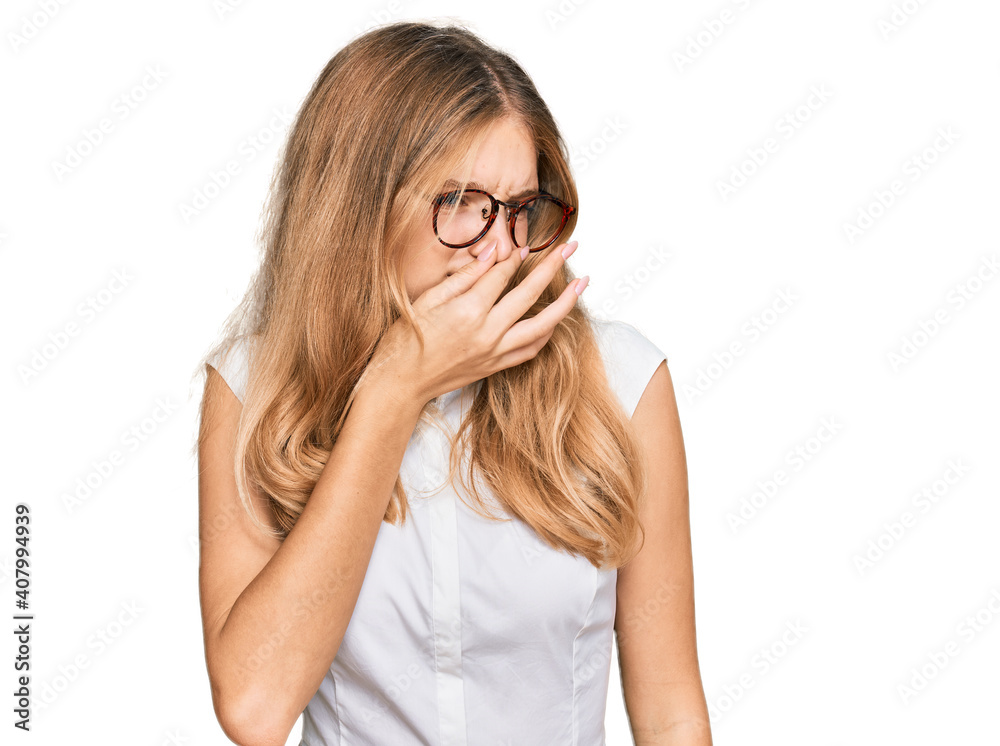Beautiful young caucasian girl wearing casual clothes and glasses smelling something stinky and disgusting, intolerable smell, holding breath with fingers on nose. bad smell Beautiful young caucasian girl wearing casual clothes and glasses smelling something stinky and disgusting, intolerable smell, holding breath with fingers on nose. bad smell
