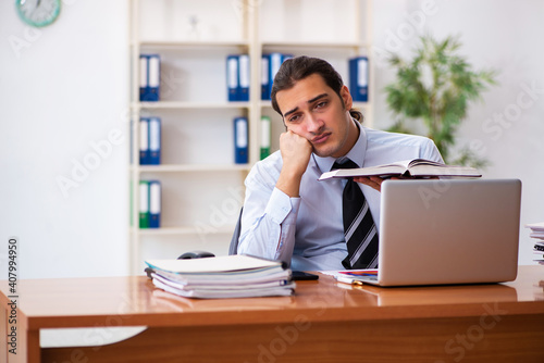 Young male student employee reading book at workplace