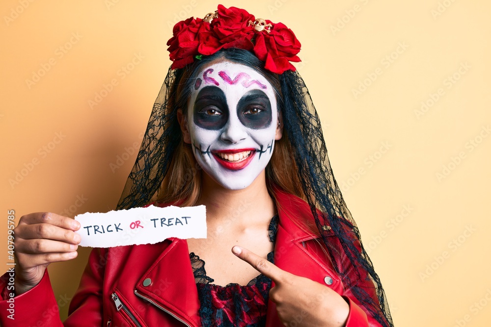 Woman wearing day of the dead costume holding trick or treat paper smiling happy pointing with hand and finger Woman wearing day of the dead costume holding trick or treat paper smiling happy pointing with hand and finger