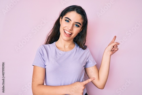 Brunette teenager girl wearing casual clothes smiling and looking at the camera pointing with two hands and fingers to the side.