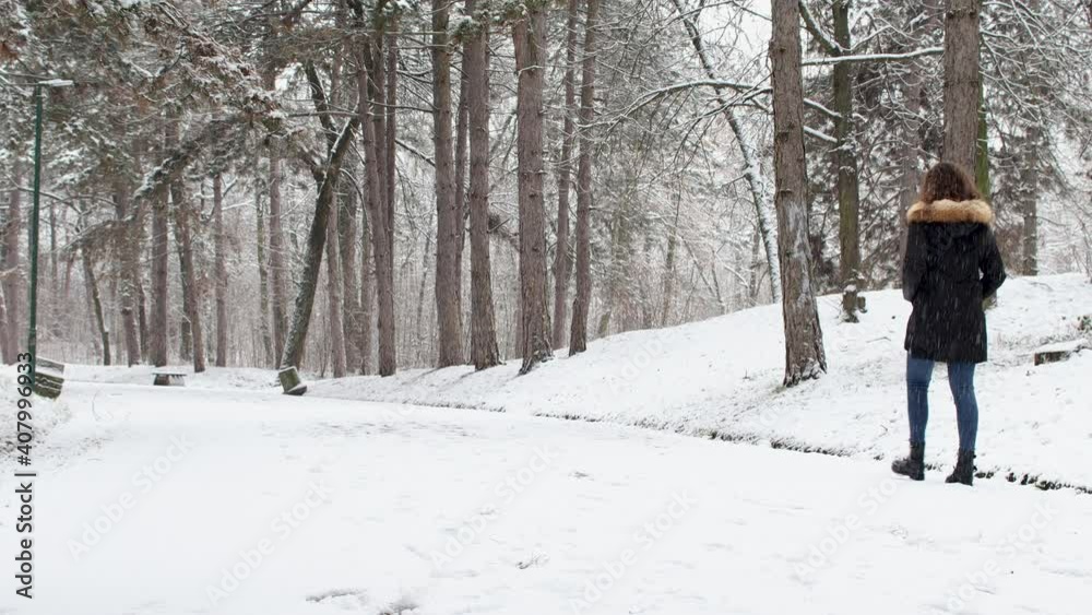 Woman walking on trail covered by snow in forest in winter season Woman walking on trail covered by snow in forest in winter season