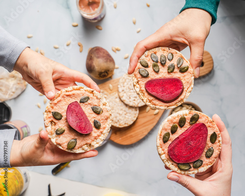 Crispy puffed rice cakes on table hummus spread and tomato and beet vegetables and sesame pumpkin seeds on the table - top view on hands holding healthy vegetarian or vegan breakfast gluten free