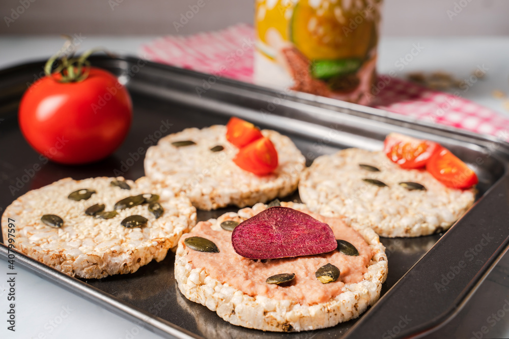 Crispy puffed rice cakes on table hummus spread and tomato and beet vegetables and sesame pumpkin seeds on the table - close up view on healthy vegetarian or vegan breakfast gluten free Crispy puffed rice cakes on table hummus spread and tomato and beet vegetables and sesame pumpkin seeds on the table - close up view on healthy vegetarian or vegan breakfast gluten free