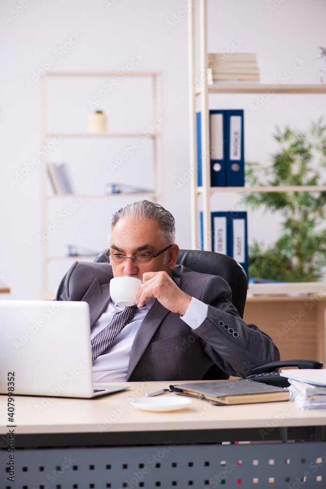 Old male employee drinking coffee in the office Old male employee drinking coffee in the office