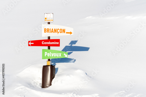 Pointer sign at mountains with snow in winter, Brianson, Alps, France. Crossroad sign in the Alps pointing to cities. Colorful directional board post at ski resort on sunny winter day photo