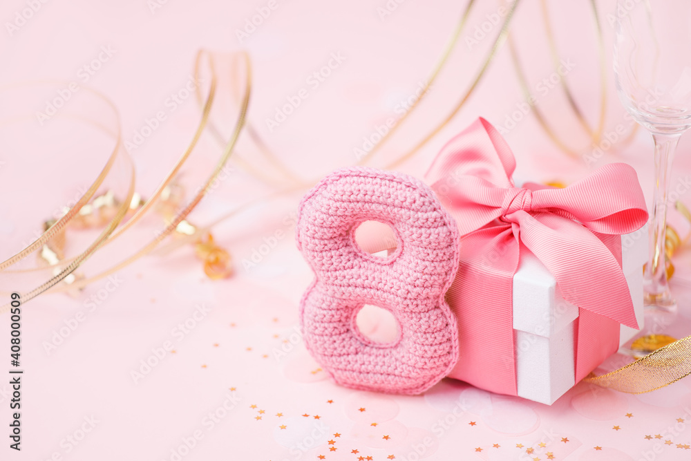 8 March, International Women's Day concept. Figure eight of pink crochet with luxury gift box, big bow on pink background. Space for text, monochrome seasonal holiday greeting card