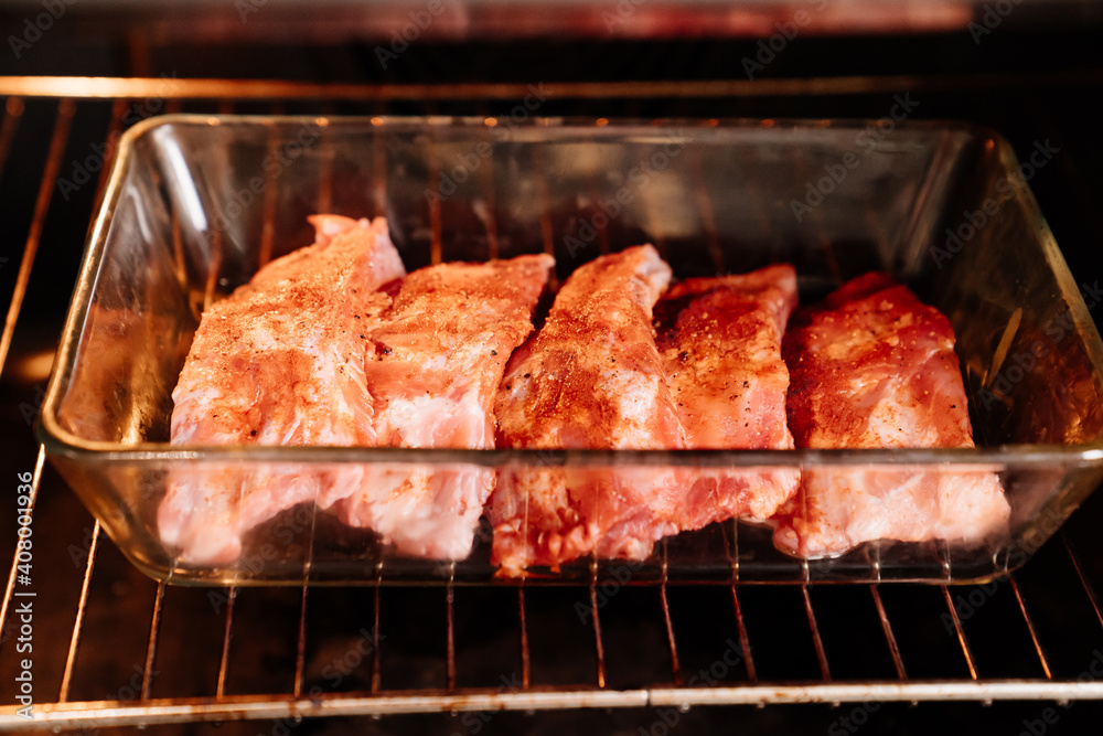 raw pork ribs sprinkle with salt, black pepper and paprika in a glass baking tray in the oven. cooking meat at home. Cook.