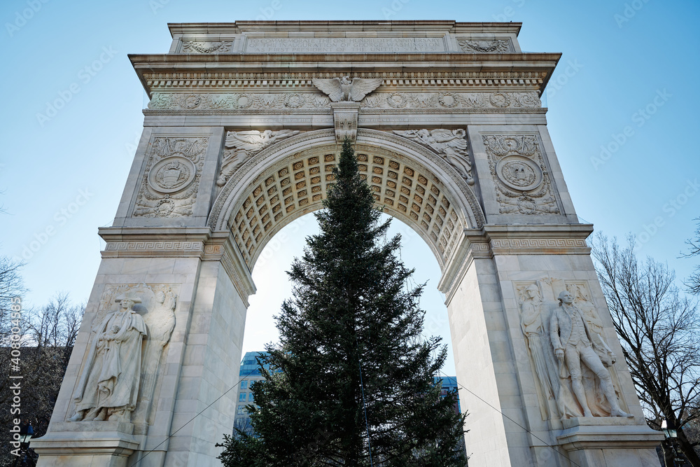 wide angle view of Washington Square Arch and Chritsmas tree from ground up to clear blue sky. The Tuckahoe marble bas relief details show an eagle, two coats of arms and statues.