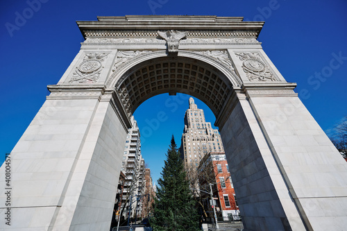 wide angle view of Washington Square Arch from ground up to clear blue sky. The Tuckahoe marble bas relief details show an eagle and two coats of arms. Midtown New York skyscrapers in background.