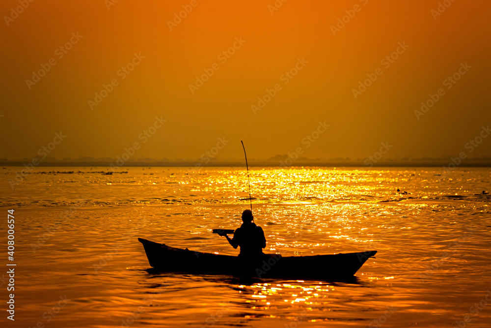 Evening golden sunset time, a fisherman fishing on the seaside on a boat.