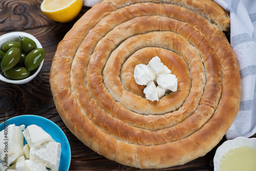 Spanakopita or greek spiral pie made of filo dough, studio shot on a brown rustic wooden background