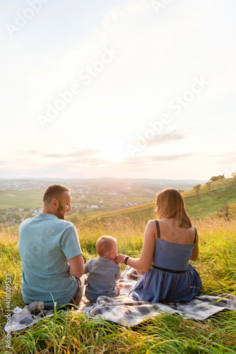 Rear view of joyful happy family sitting together at outdoor looking on sunset © Oleh