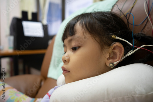 A little girl is wearing a hearing aid and is doing a neurofeedback exam. Making EEG electrodes.