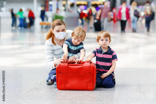 Young mother with two little kid boys at airport. Cute preschool children, siblings, twins and woman, family traveling together, going on vacation via airplane. Waiting for flight at the terminal