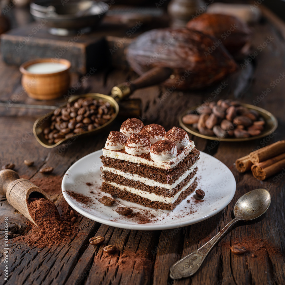 Slice of chocolate cake with tiramisu cream and cocoa powder on wooden table. - obrazy, fototapety, plakaty 