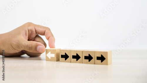 Close-up hand choose cube wooden toy block with arrow icon pointing to opposite directions for business change leader to growth and planning company strategies change and transform to success concept.