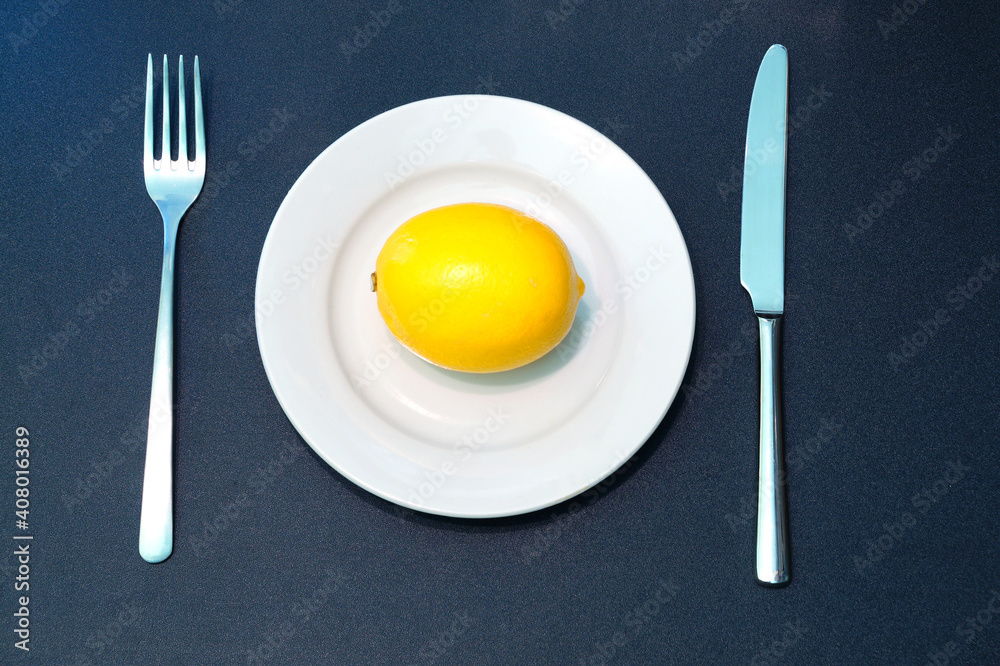 Yellow lemon on white plate with knife and fork.