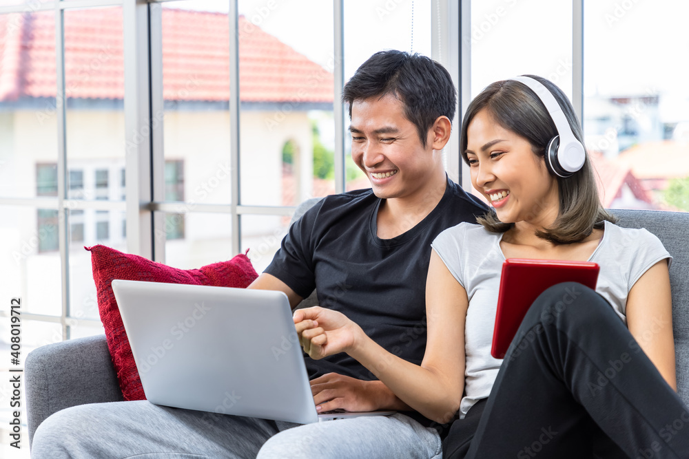 Young Asian couple relaxing sitting on sofa using laptop computer and digital tablet working from home Young Asian couple relaxing sitting on sofa using laptop computer and digital tablet working from home