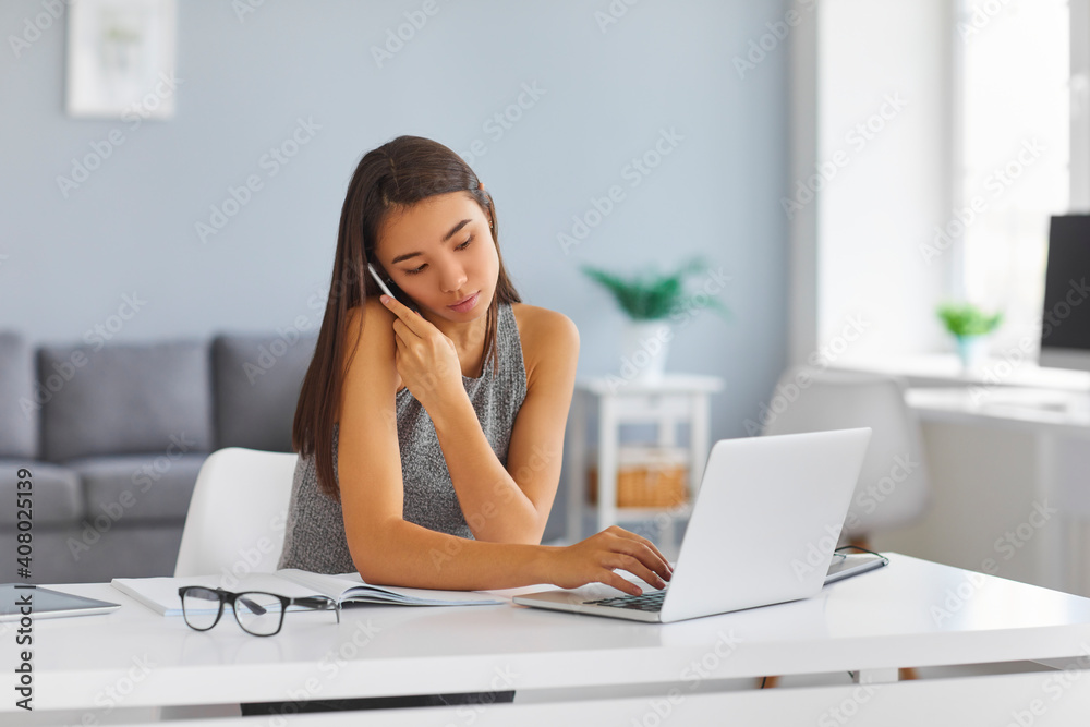 Serious busy young woman making call and typing on laptop keyboard at the same time Serious busy young woman making call and typing on laptop keyboard at the same time