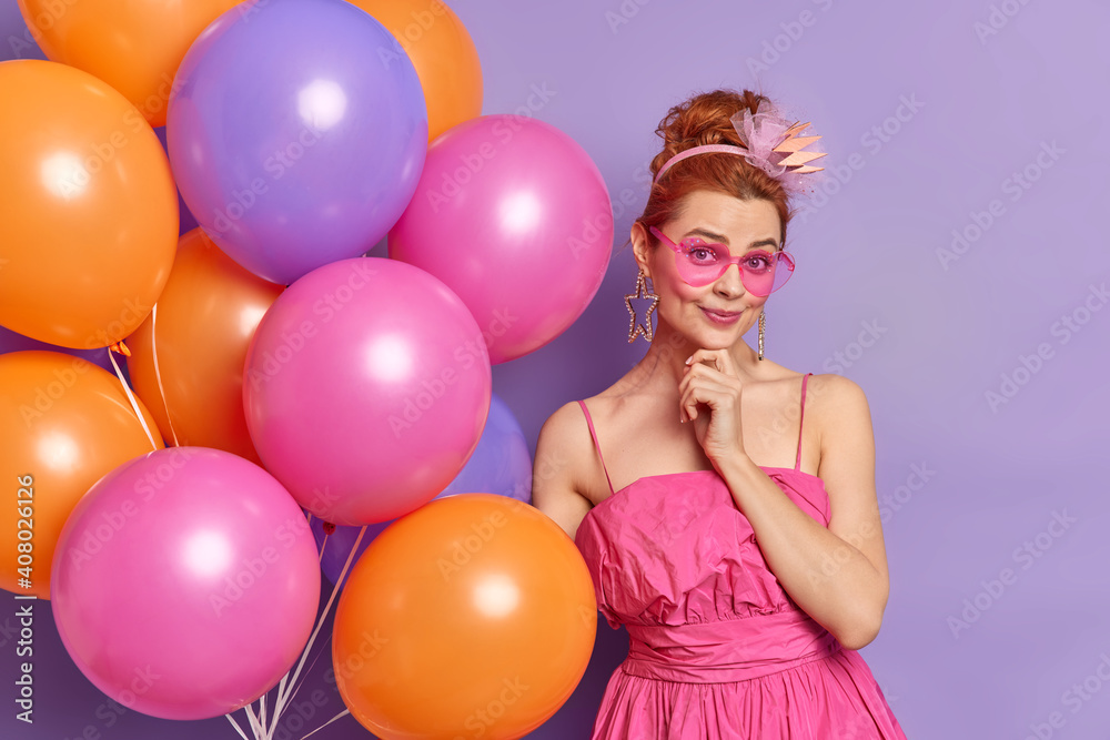 Obraz premium People celebration and holidays concept. Fashionable nineties woman looks gladfully at camera wears clothes in vintage style prepares for party poses with balloons isolated over purple background